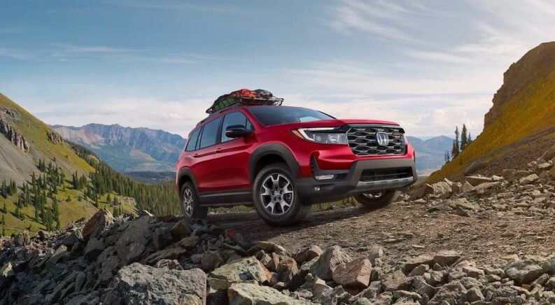 A red 2023 Honda Passport TrailSport is shown driving up a gravel mountain trail.