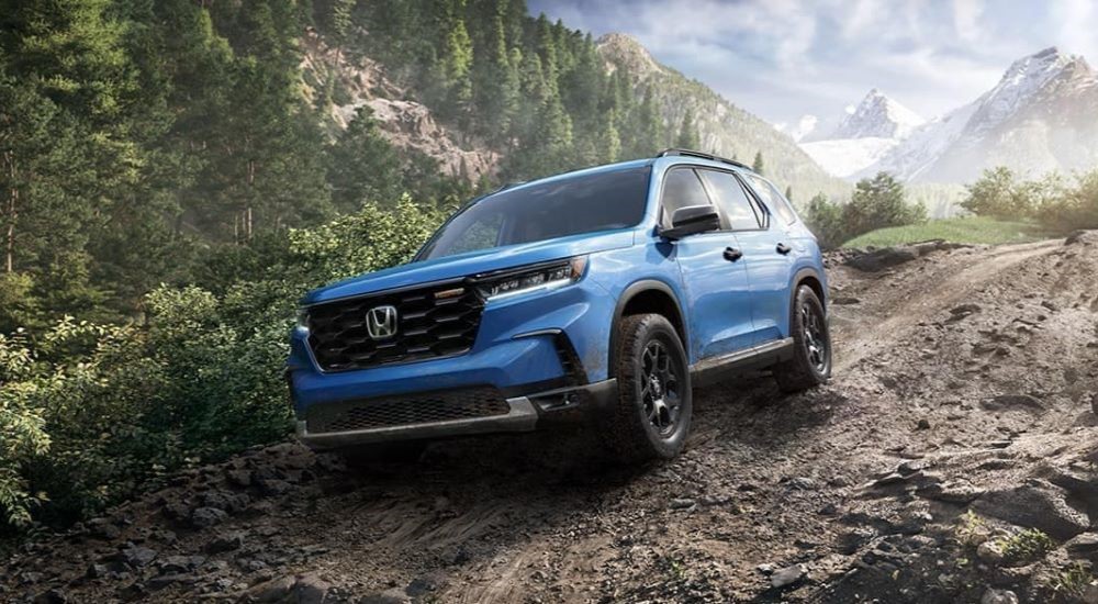 A blue 2023 Honda Pilot TrailSport is shown off-roading through the mountains.