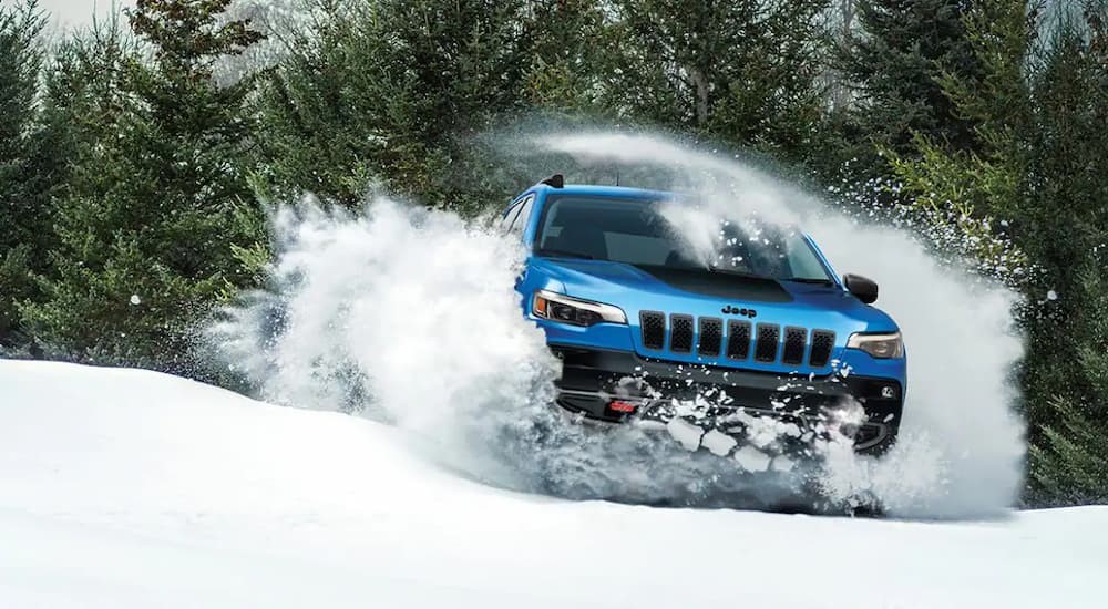 A blue 2023 Jeep Cherokee Trailhawk is shown driving through the snow.