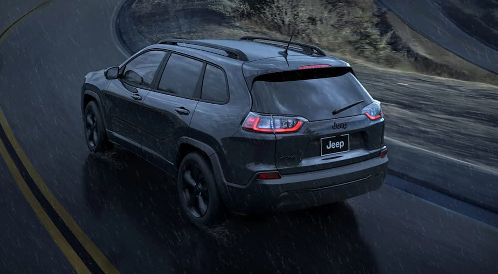 A black 2023 Jeep Cherokee Altitude Lux is shown from the rear driving in a rain storm.