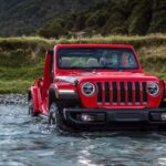 A red 2023 Jeep Wrangler Rubicon is shown driving through a lake.
