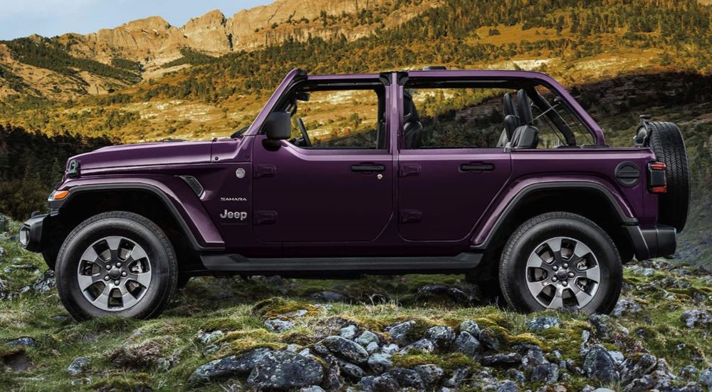 A popular Jeep Wrangler for sale near you, a purple 2023 Jeep Wrangler Sahara, is shown from the side while off-roading. 