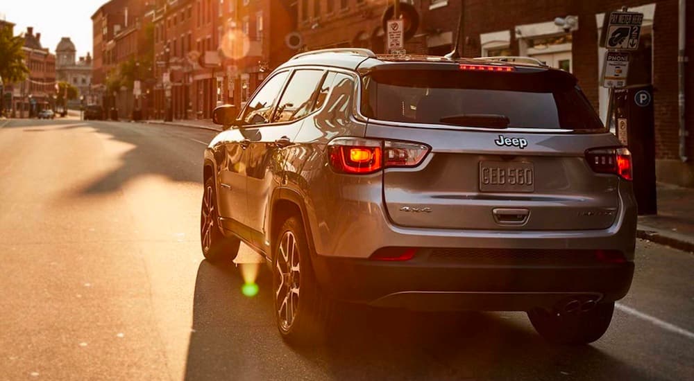 A silver 2021 Jeep Compass is shown driving down a city street into the sunset.