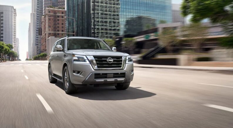 A silver 2023 Nissan Armada is shown driving on a road near a city.