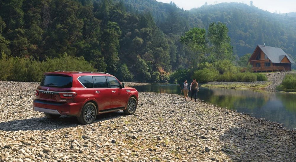 A red 2023 Nissan Armada Platinum is shown parked off-road near a stream.