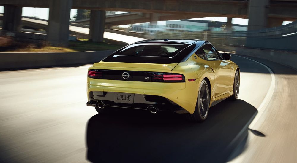A yellow 2023 Nissan Z is shown from the rear speeding along a highway curve under a bridge. 