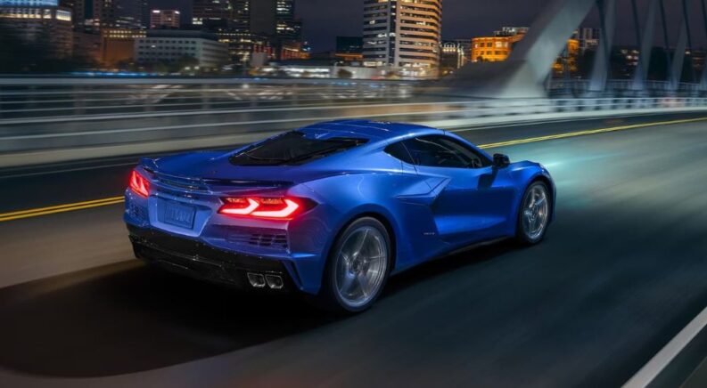 A blue 2024 Chevy Corvette E-Ray is shown speeding down a highway street at night.