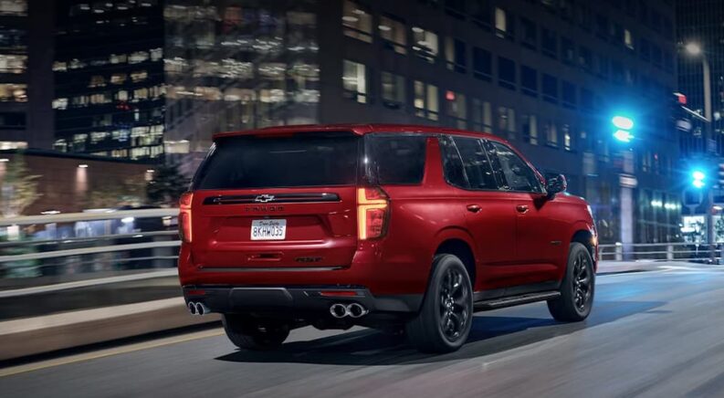A red 2023 Chevy Tahoe RST is shown driving down a city street at night after leaving a Chevy dealer.