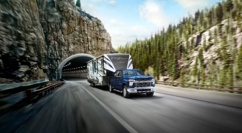 A blue 2022 Chevy Silverado 2500 HD is shown pulling a fifth-wheel camper through a tunnel.