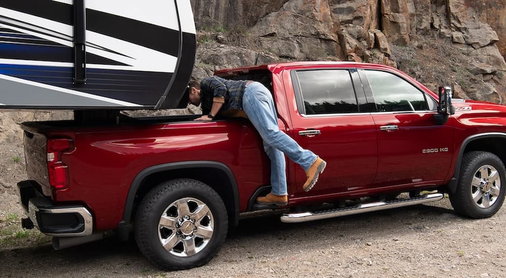 A man is shown climbing into the bed of a red 2023 Chevy Silverado 2500 HD to connect a fifth-wheel hitch.
