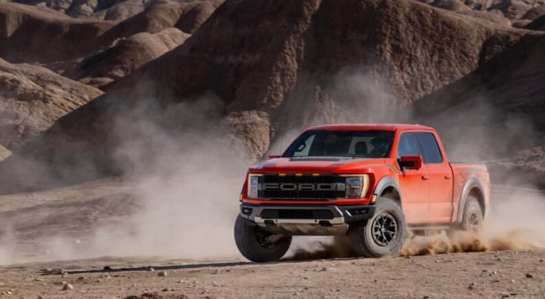 A red 2023 Ford F-150 Raptor is shown kicking up dust in the desert after leaving a Ford F-150 dealer.
