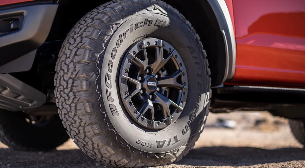 An all-terrain tire and beadlock wheel are shown on a red 2023 Ford F-150.