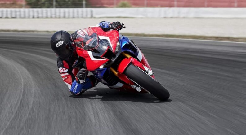 A red, white, and blue 2021 Honda CBR1000RR-R Fireblade SP, the top Honda CBR for sale, is shown cornering at the track.