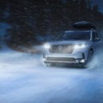 A white 2023 Honda Pilot is shown driving through a snowy country road at night after leaving a Honda dealer.