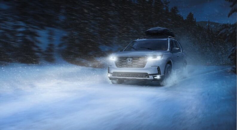 A white 2023 Honda Pilot is shown driving through a snowy country road at night after leaving a Honda dealer.