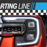 The driver side headlight is shown on an orange Ford Ranger Raptor under a Starting Line banner.