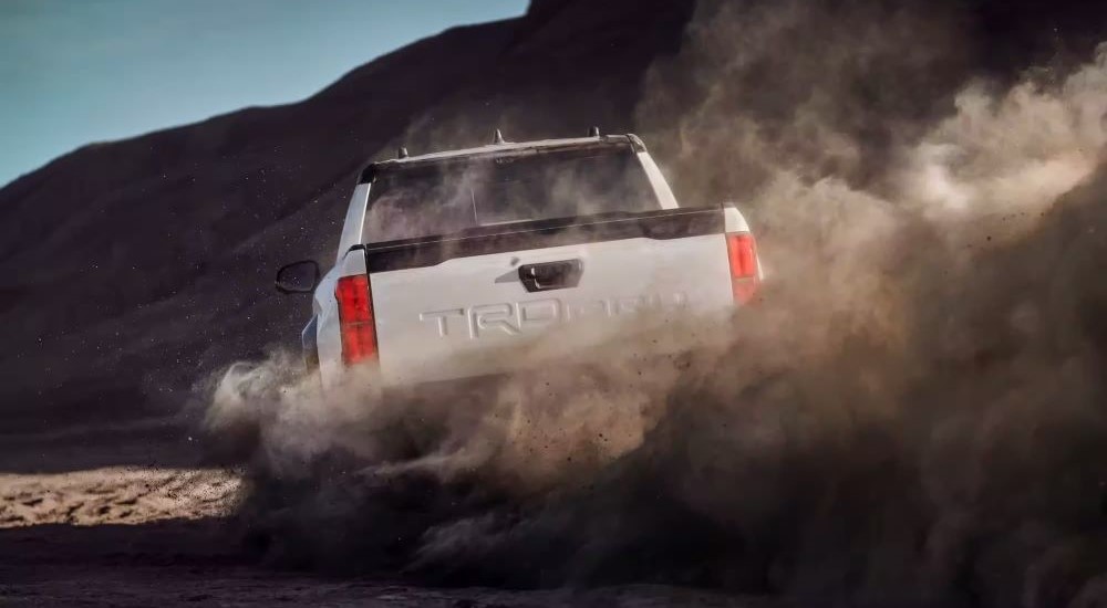 A white 2024 Toyota Tacoma TRD Pro is shown from behind kicking up dust.
