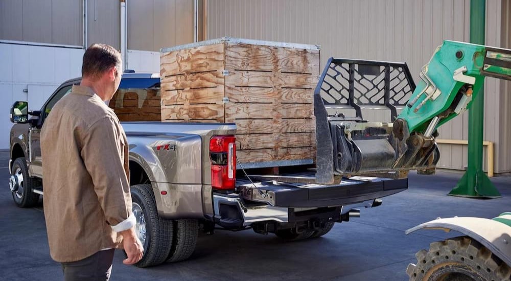 A wooden box crate is shown being loaded onto a tan 2023 Ford Super Duty F-450.