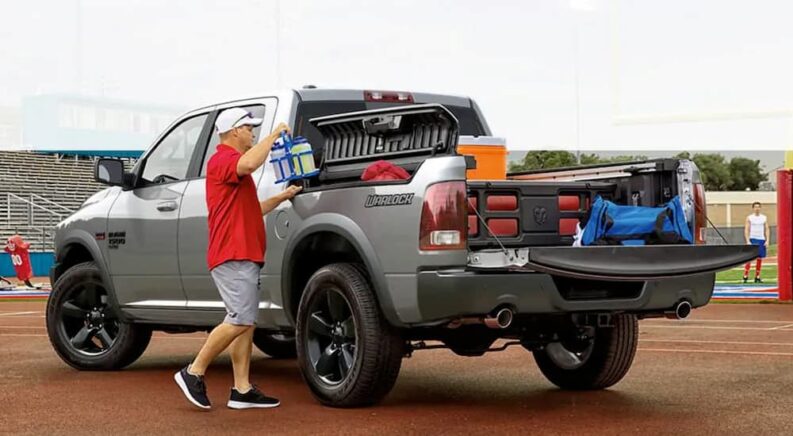 A man is shown loading a gray 2019 Ram 1500 Classic equipped with the RamBox cargo management system at a football practice.