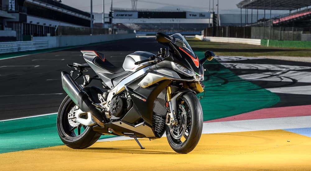 A silver and black 2022 Aprilla RSV4 is shown parked on a race track.