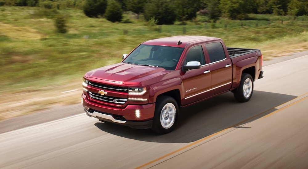 A popular used Chevy truck near me, a red 2018 Chevy Silverado, is shown driving on a highway.