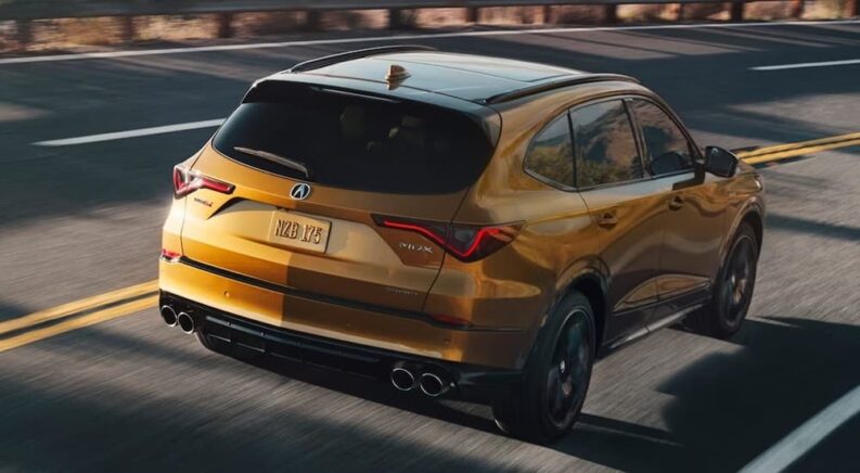 A gold 2022 Acura MDX A-Spec is shown from the rear at an angle after leaving a dealer that has used SUVs for sale.