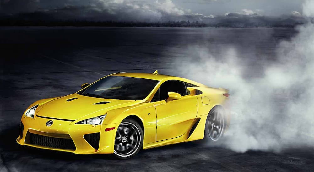 A yellow 2012 Lexus LFA is shown from the front at an angle while performing a burnout.