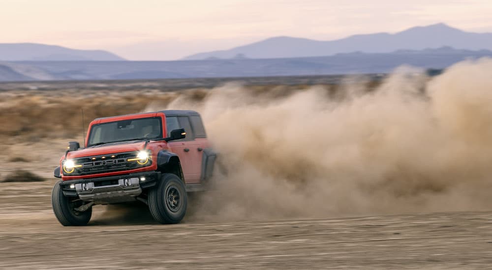 An orange 2022 Ford Bronco Raptor is shown from the front while sliding through dirt.