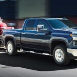 A blue 2023 Chevy Silverado 2500 HD is shown towing a red truck.