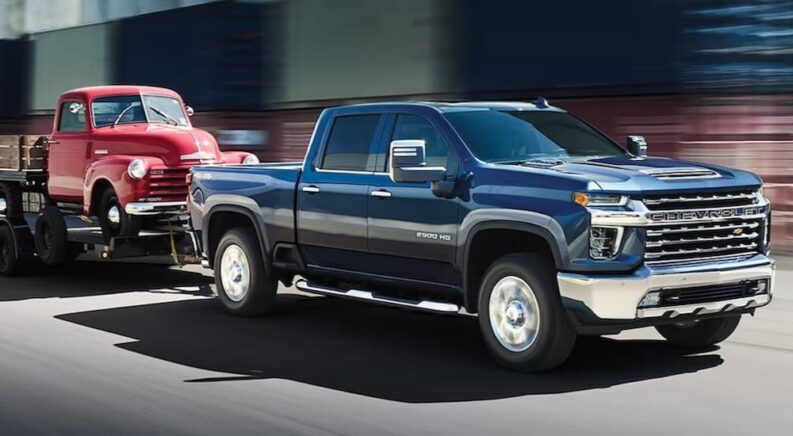 A blue 2023 Chevy Silverado 2500 HD is shown towing a red truck.