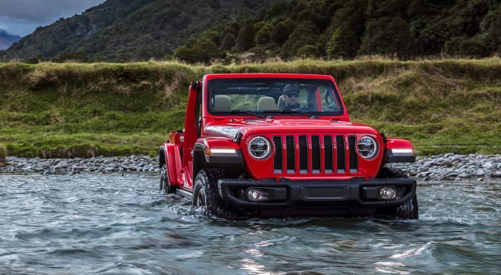 A red 2023 Jeep Wrangler Rubicon is shown off-roading through a stream.