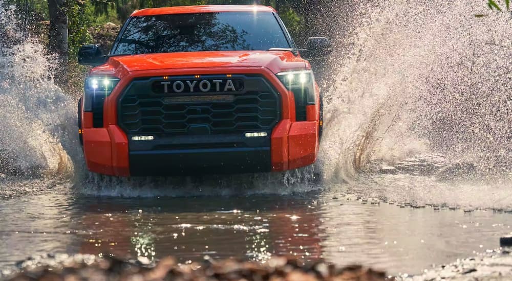 An orange 2023 Toyota Tundra is shown off-roading through water.