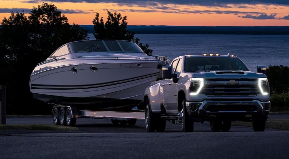 A white 2024 Chevy Silverado 2500 HD is shown towing a boat.