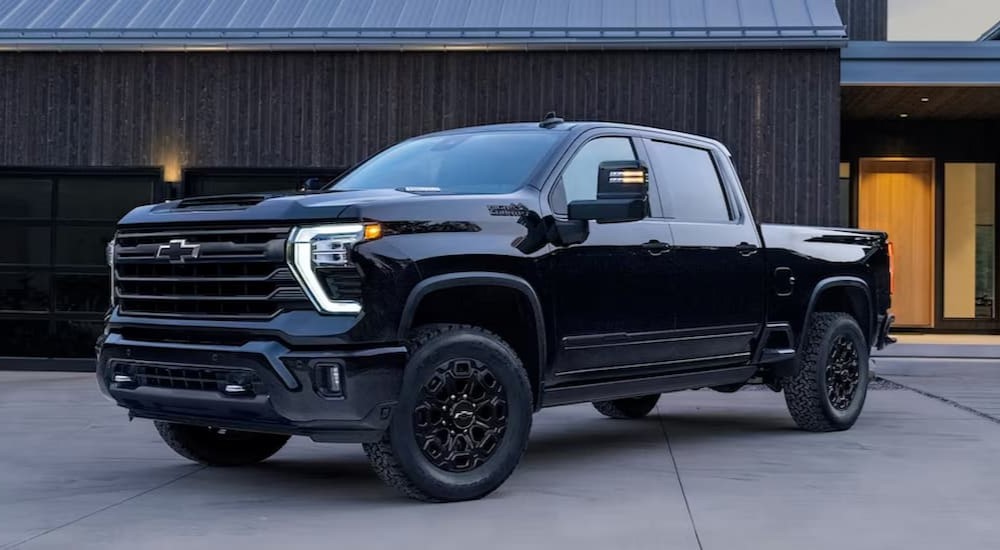 A black 2024 Chevy Silverado 2500 HD High Country is shown parked near a garage.