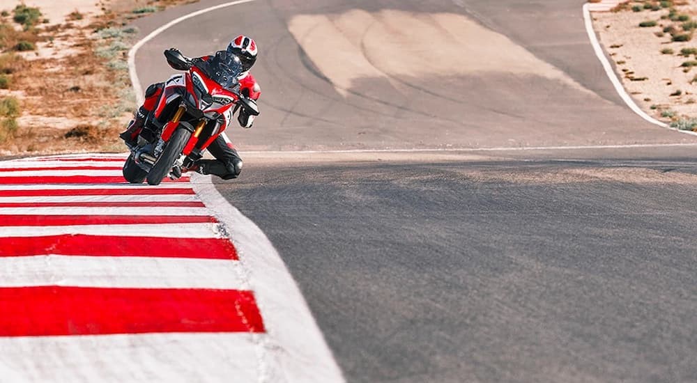 A red and white Ducati Multistrada V4 Pikes Peak is shown riding on a racetrack. 