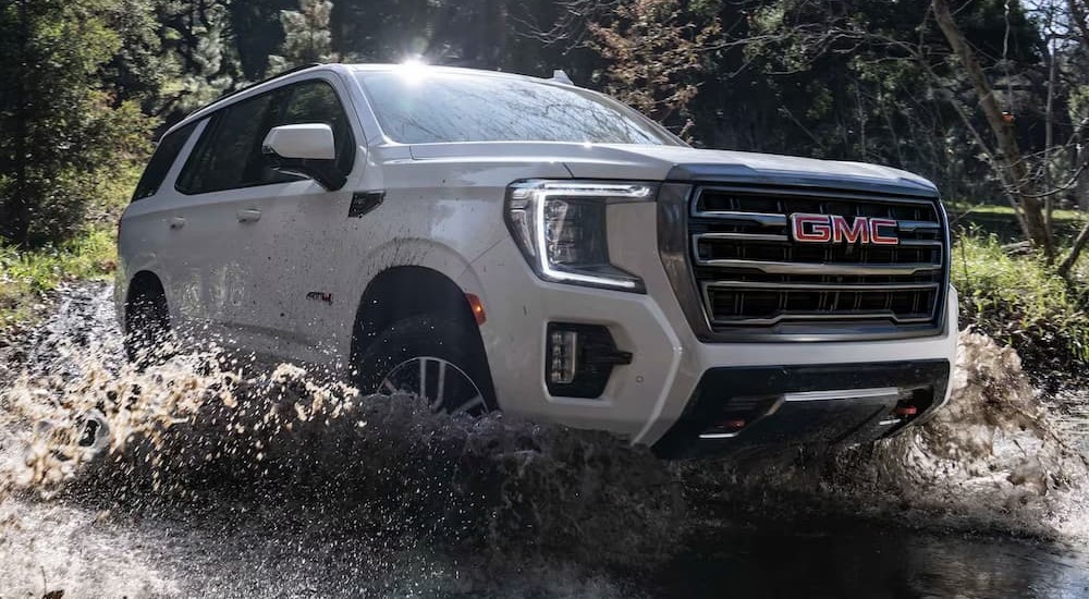 A white 2023 GMC Yukon AT4 is shown driving through water.