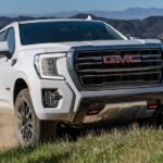 A white 2023 GMC Yukon AT4 is shown off-roading after visiting a GMC dealer.