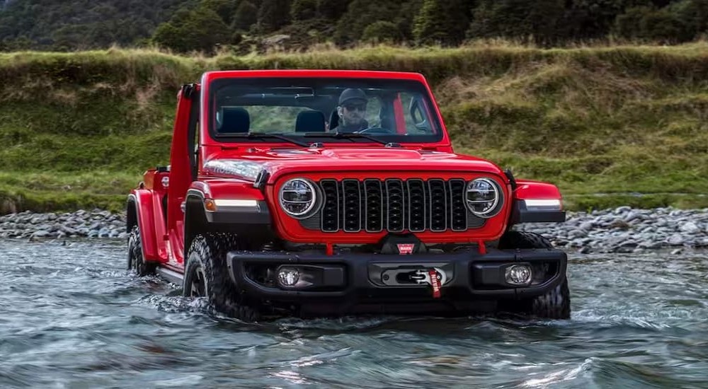 A red 2024 Jeep Wrangler Rubicon is shown off-roading through water.