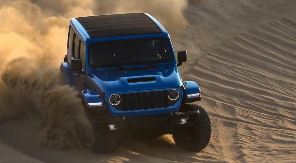 A blue 2024 Jeep Wrangler Rubicon is shown driving on sand.