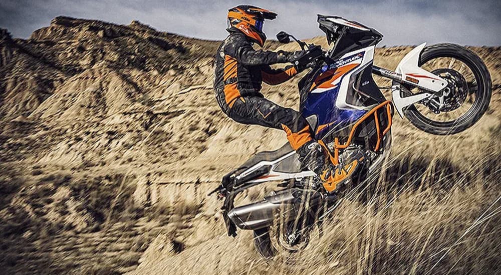 A blue and white KTM 1290 Super Adventure R is shown riding off-road.