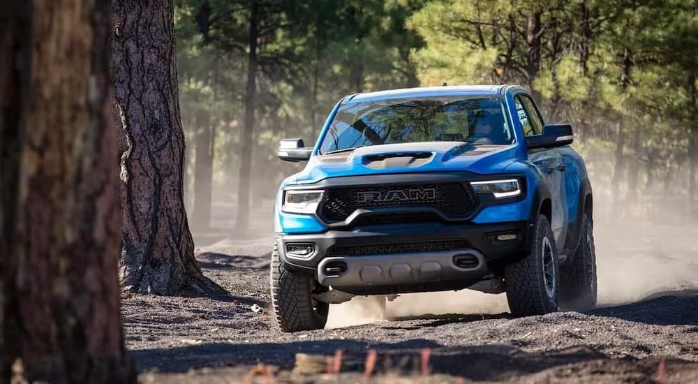 A blue 2023 Ram 1500 TRX is shown driving off-road near trees.