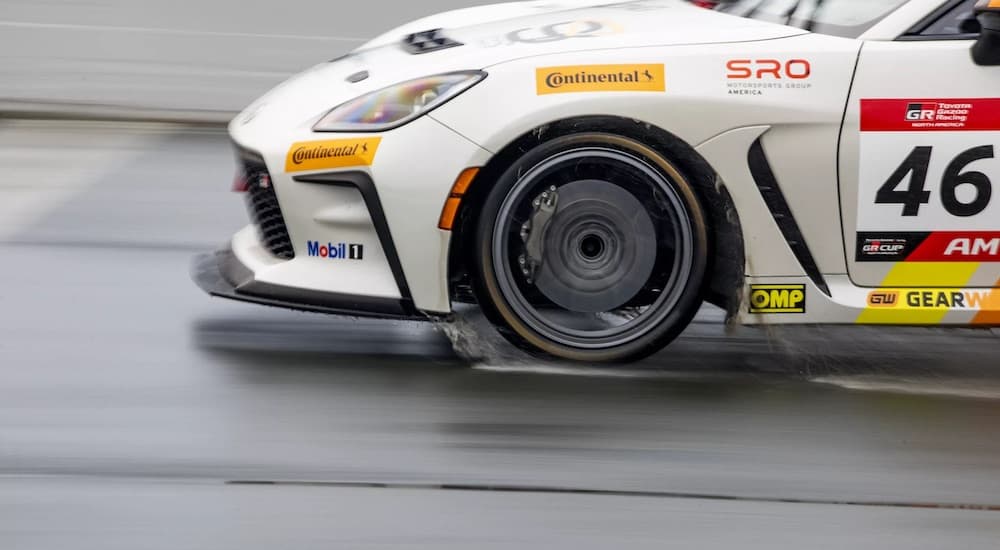 A white Toyota GR cup car is shown from the side while driving in the rain.