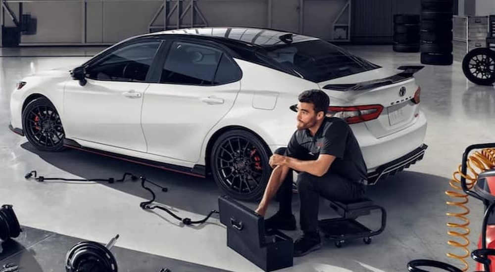 A mechanic is shown sitting near a white 2022 Toyota Camry TRD.