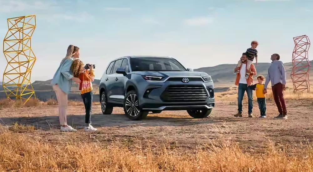 A family is shown near a blue 2024 Toyota Grand Highlander.