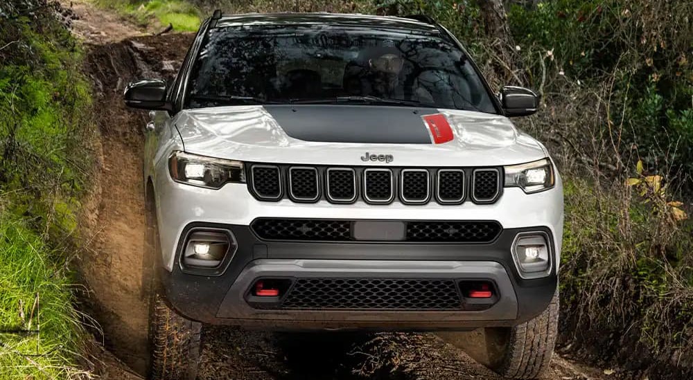 A white and black 2023 Jeep Compass Trailhawk is shown driving off-road after visiting a used Jeep dealer.