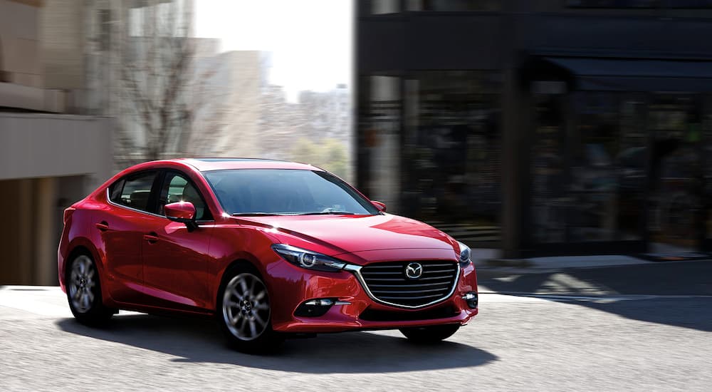 A red 2018 Mazda 3 is shown driving on a road.