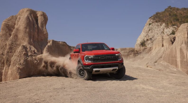 An orange 2024 Ford Ranger Raptor is shown from the front while off-road.