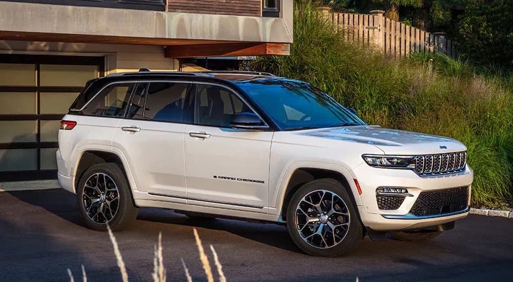 A white 2023 Jeep Grand Cherokee is shown from the side while parked in a driveway.