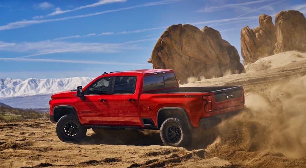A red 2024 Chevy Silverado 2500 HD ZR2 Bison is shown driving off-road on dirt.