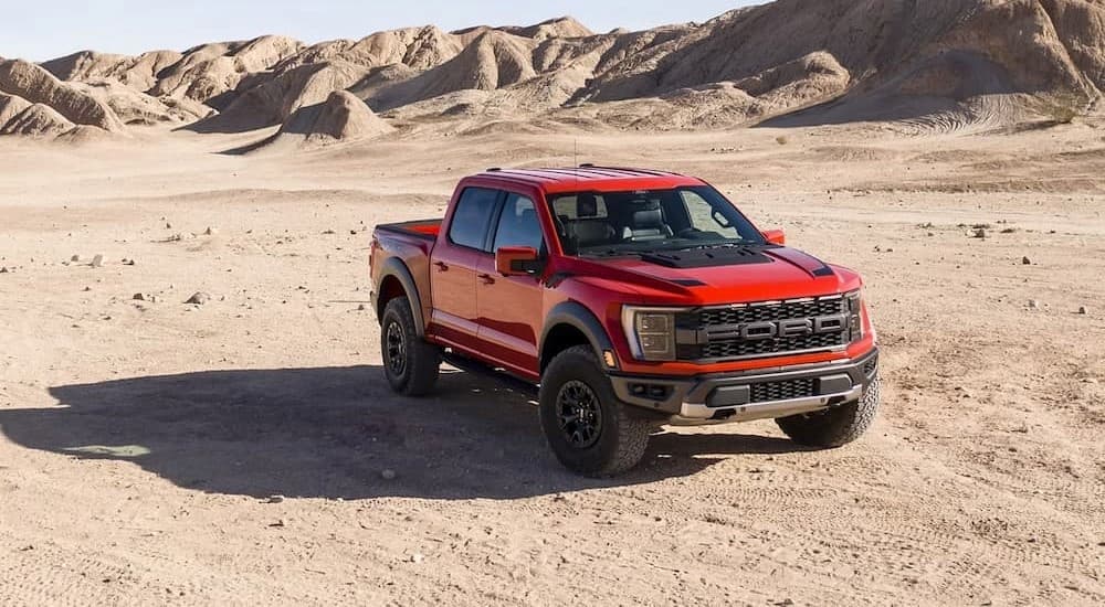 A red 2023 Ford F-150 Raptor is shown parked off-road on dirt.